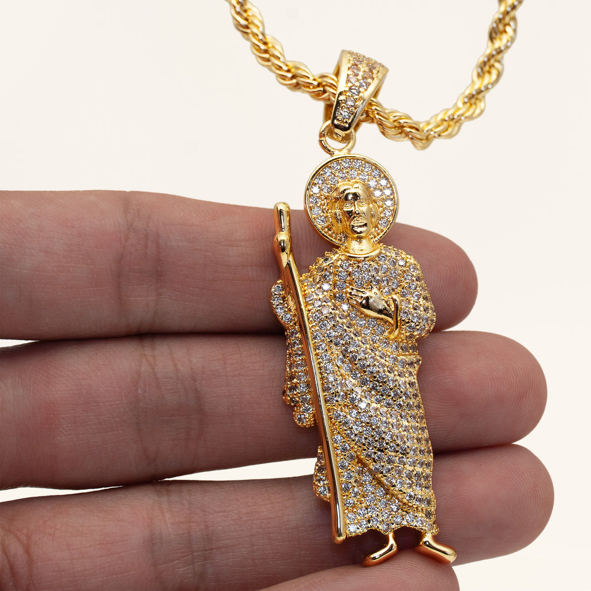 Dije de San Judas Tadeo con circonitas blancas en la mano para mostrar su tamaño