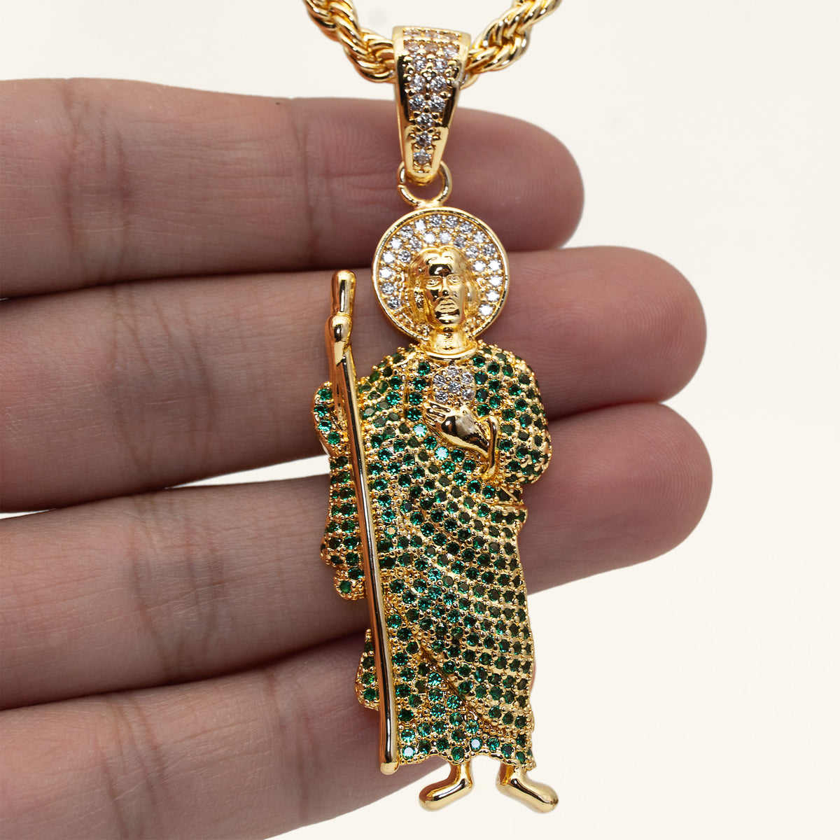 Dije de San Judas Tadeo con circonitas verdes en la mano para mostrar su tamaño